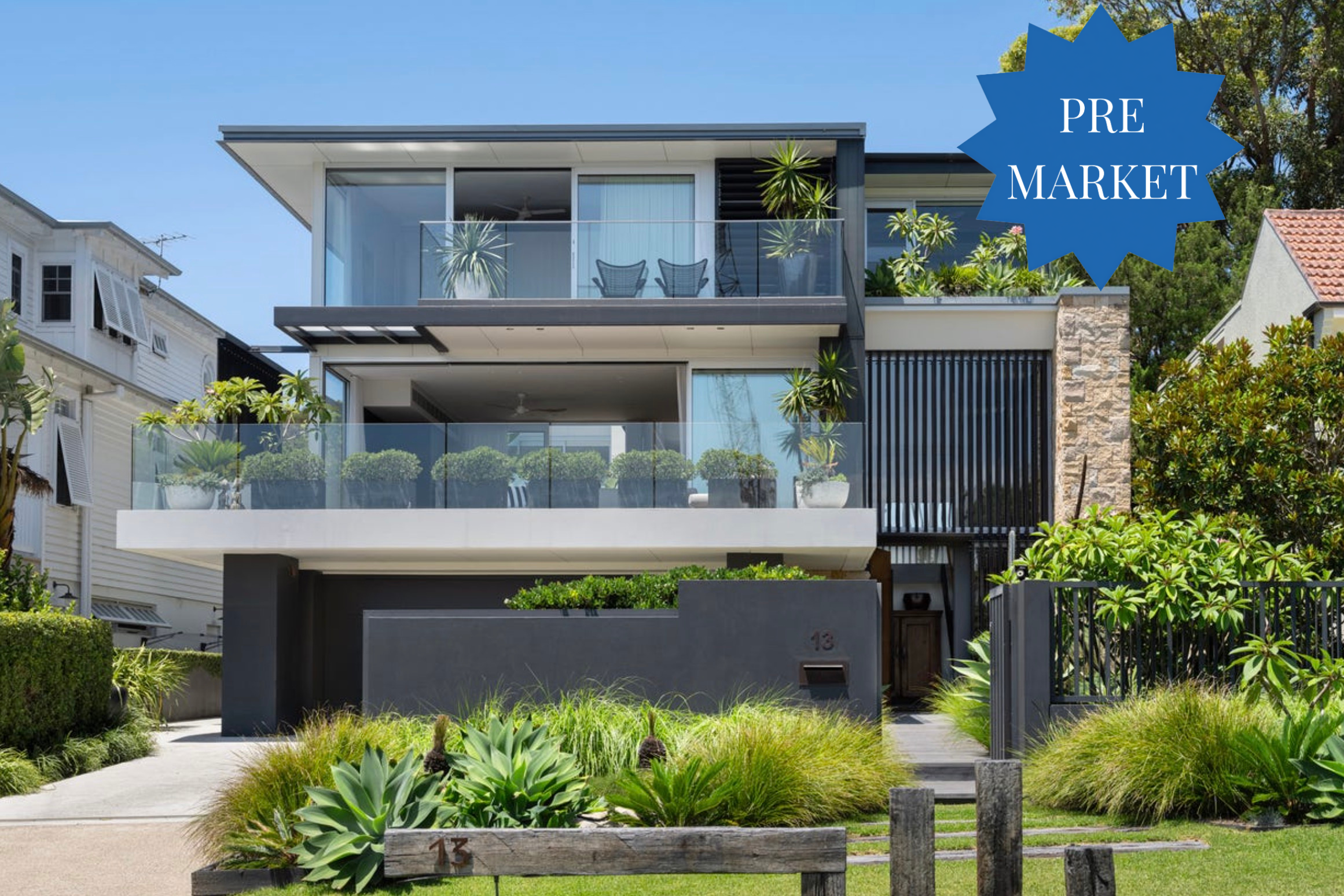 Modern multi-story home with glass balconies, lush plants, and a large blue PRE MARKET badge in the upper-right corner.