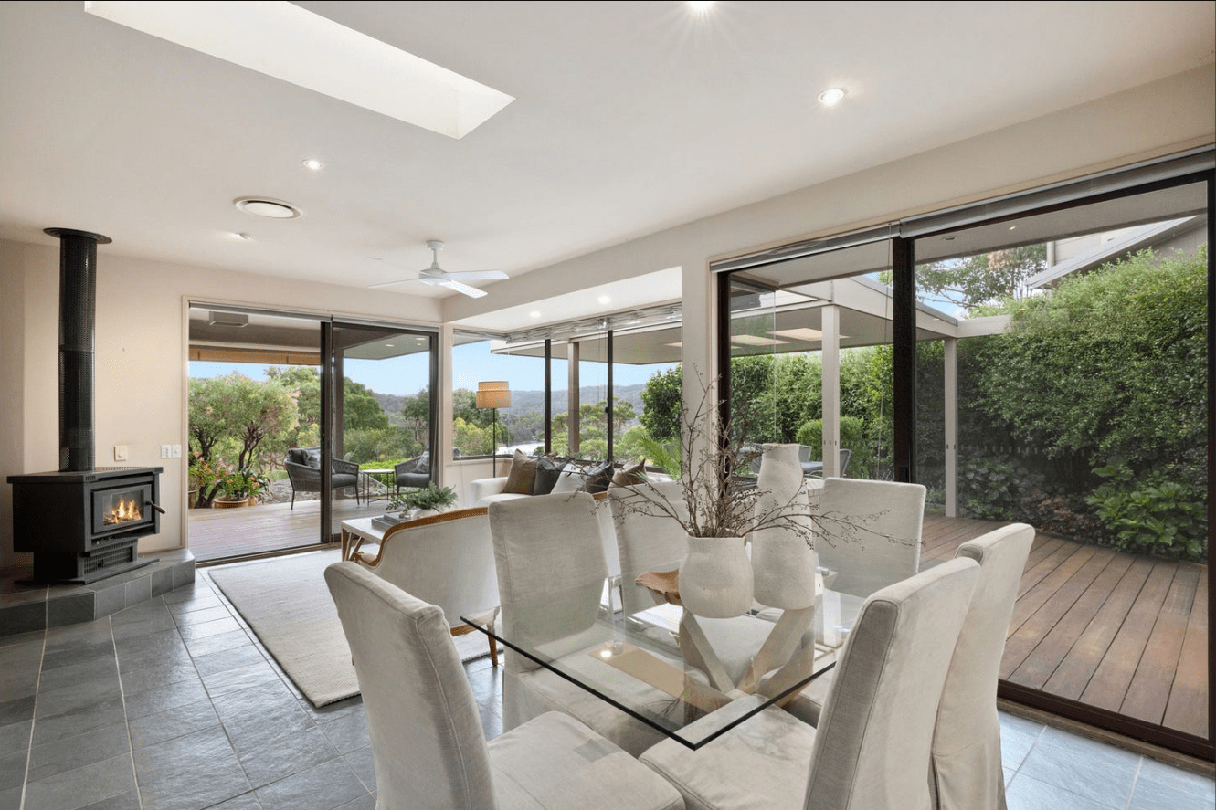 Modern dining and living area with glass table, white chairs, and garden view by Buyers Agent seaforth.