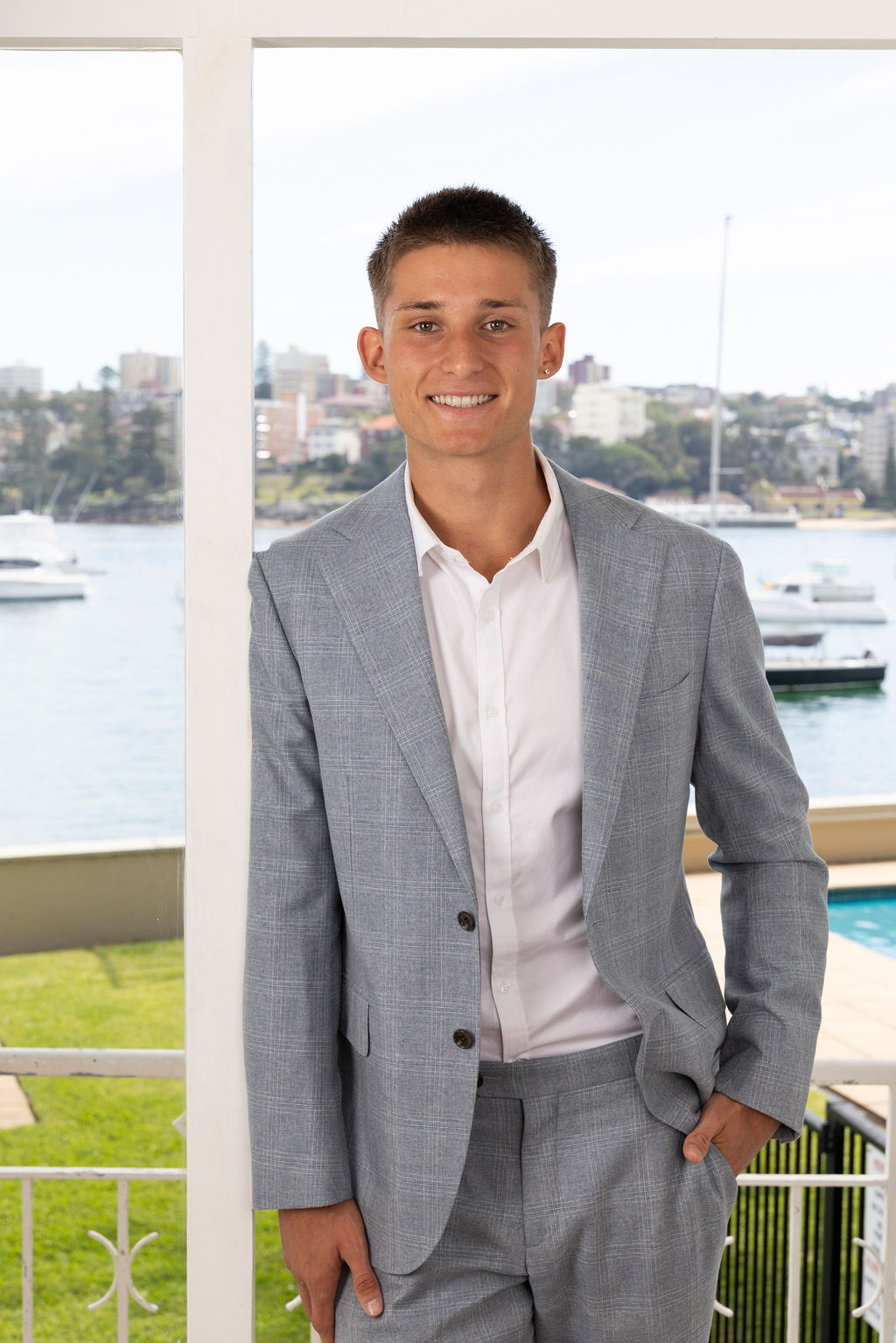 Associate Buyer’s Agent Luke Black in a gray suit by the water, with boats and cityscape in the background.