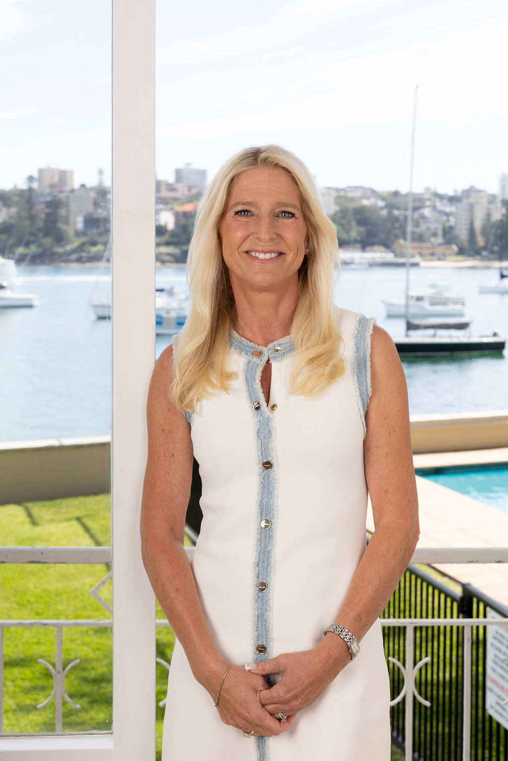 Katarina Rossel, Senior Buyer’s Agent, stands in a white dress by water and boats, ready to help home buyers.
