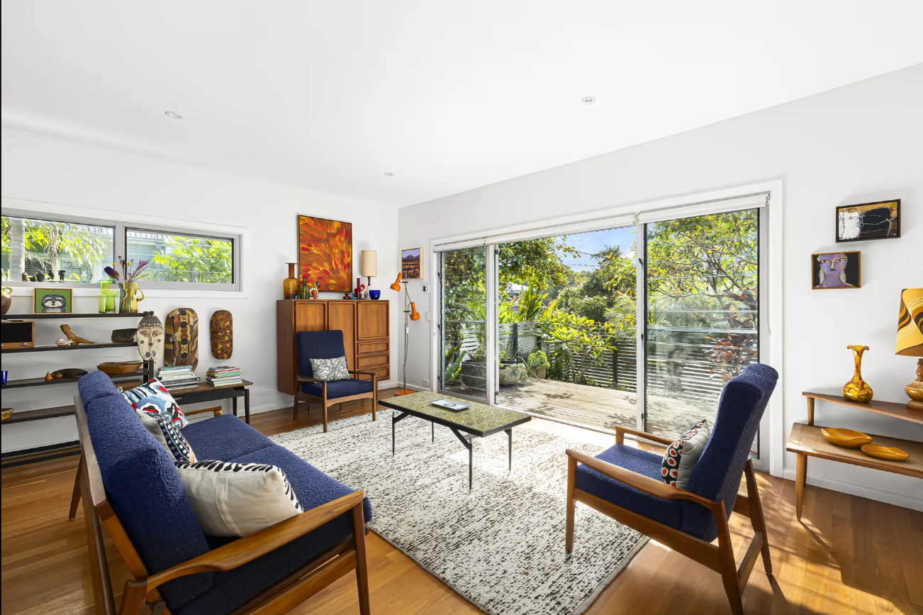 Living room with midcentury seating, wooden furniture, and a large sliding glass door opening to a sunny garden.