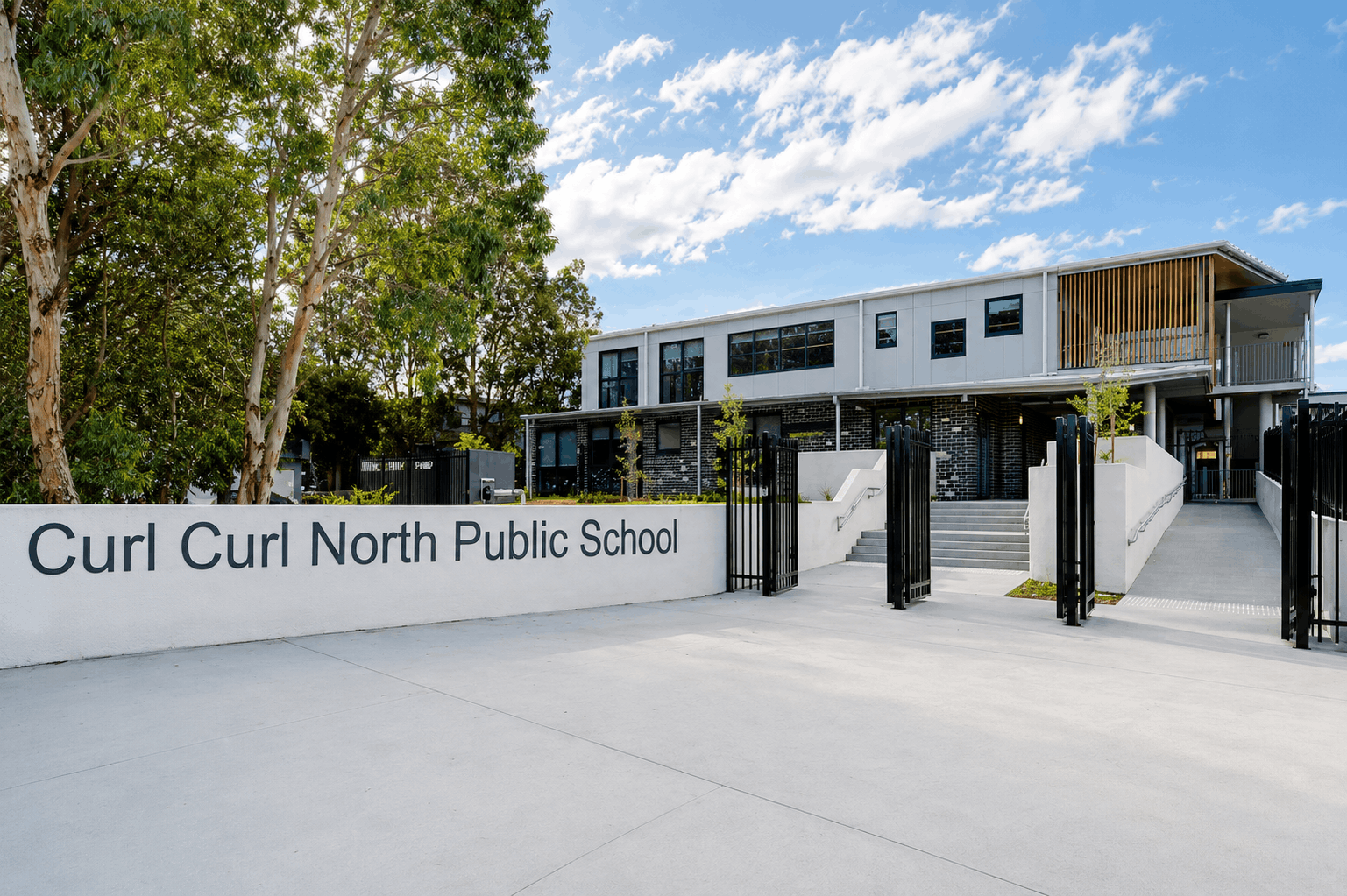 Exterior view of Curl Curl North Public School with modern design, large windows, and lush trees outside.