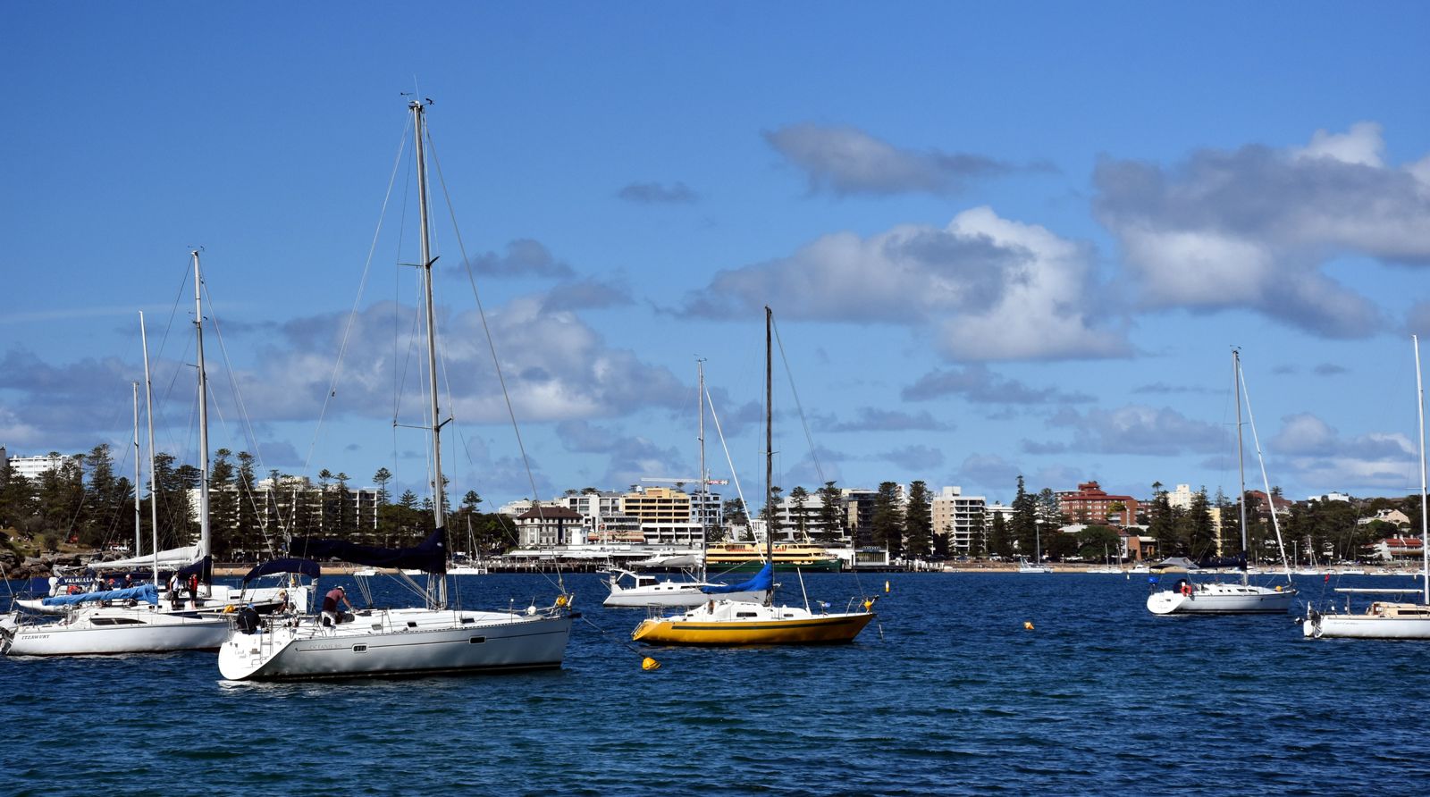 Small boats on grassy shore by wooden pier at Forty Baskets Beach, with sailboats and houses across the bay.